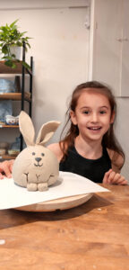 Niña mostrando su pieza de cerámica hecha en el taller.