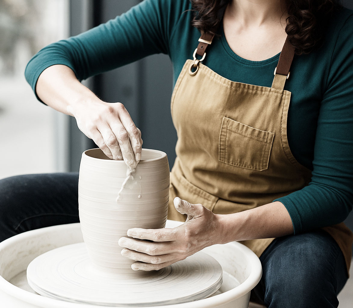 Mujer modelando una pieza de arcilla en el torno de alfarería con las manos.