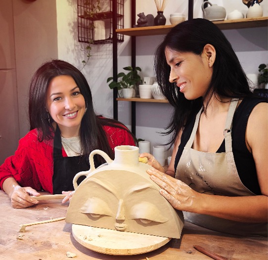 Profesora guiando a una alumna en una clase mensual de cerámica.